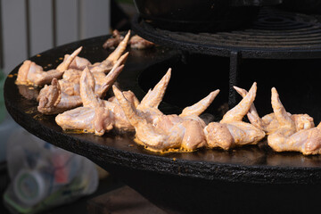 Marinated chicken wings placed on hot circular grill over embers at outdoor food festival,...