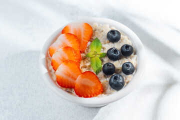 Strawberry blueberry oatmeal with mint leaves on sunny table