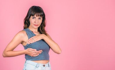 Young woman performing self-breast exam against pink background with copy space