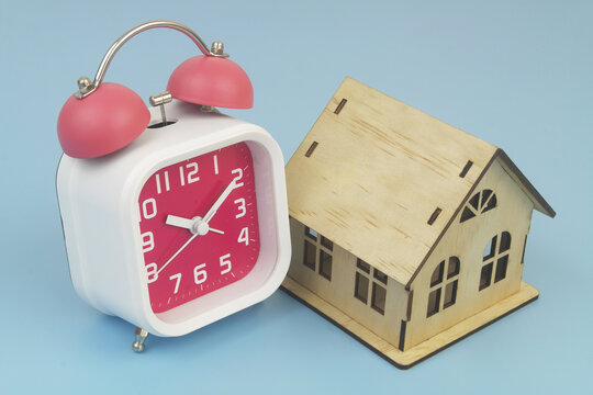 Alarm clock and wooden house  model on blue  background.