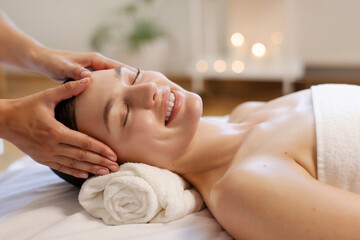 Happy woman receiving relaxing head and facial massage at luxury spa in serene candlelit...