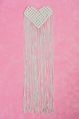 Heart shaped macrame piece with long fringe on pink background