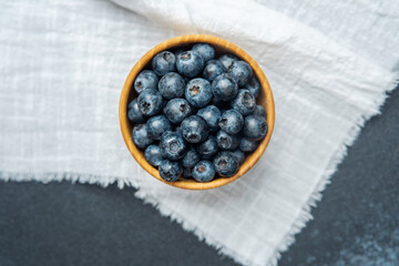 Fresh blueberries in a wooden bowl on a white cloth backdrop