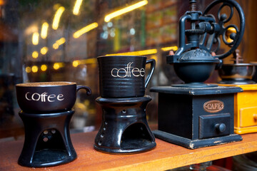 Vintage coffee mugs and traditional manual coffee grinder on wooden shelf, with warm bokeh lights...