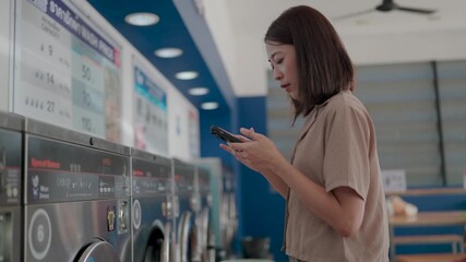 A focused individual stands in a modern laundromat engrossed in their smartphone representing everyday convenience and efficiency. - Powered by Adobe
