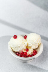Vanilla ice cream scoops in bowl with fresh red currants on light background
