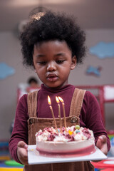 Africa American boy hold on celebrating her birthday cake and blow candles on cake in Kids birthday celebratiion party.