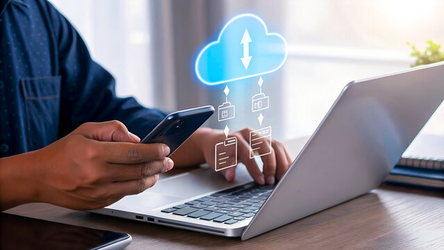 A person works at a desk with a smartphone and laptop, interacting with a translucent cloud icon floating above the devices