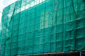 A building enveloped in green construction netting, symbolizing progress and urban development. The...