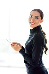 Confident young woman in sportswear using smartphone while indoors with natural daylight