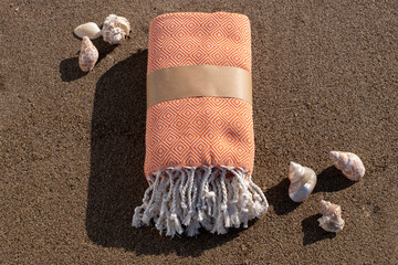 Folded beach towel and seashells on sand. Summer beach accessories on sandy background. Packed...