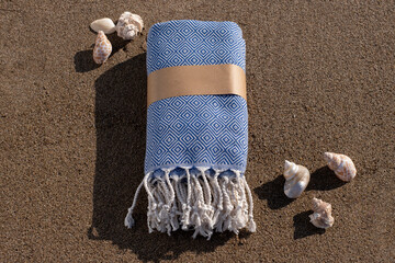 Folded beach towel and seashells on sand. Summer beach accessories on sandy background. Packed...