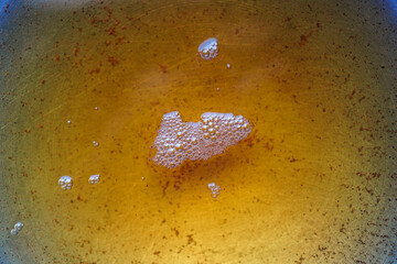 Detailed top-down close-up displaying a viscous gold liquid, filled with small bubbles and residue....
