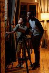 Modern African American father and his lovely son spending evening together at home watching stars...