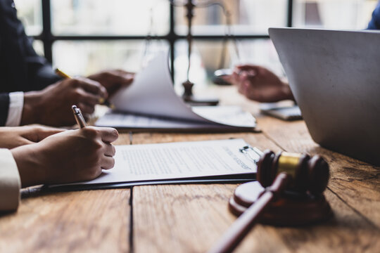 Lawyers and clients reviewing contract agreement terms before signing. Business partners carefully review contract terms before signing at a wooden table.