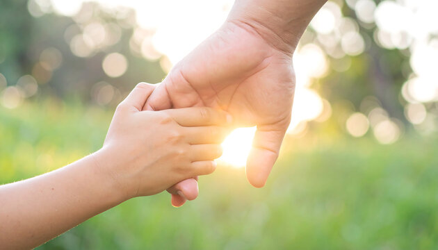 Adult and child hands clasped together, bathed in warm sunlight, symbolizing care and connection in a natural outdoor setting.