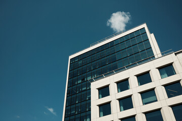 Modern office building with glass facade against clear blue sky and a single white cloud above the rooftop. Minimalist urban architecture scene. Belgrade, Serbia