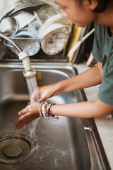 Young female person washing her hands in kitchen sink under running water from a faucet after finish washing the dishes. motion blur.