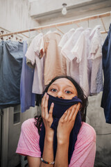 Southeast Asian teenage girl covering her face with clean washed shirt while doing her daily routine domestic chore in the laundry area