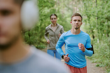 Caucasian young adult man jogging outdoors on forest path with Caucasian young adult woman...