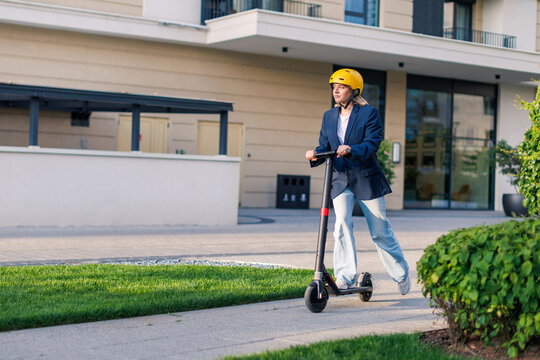 Young woman rides electric scooter on urban street wearing a yellow helmet