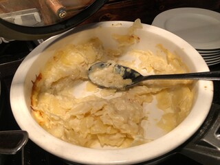 Scalloped potatoes in a white baking dish with a spoon.