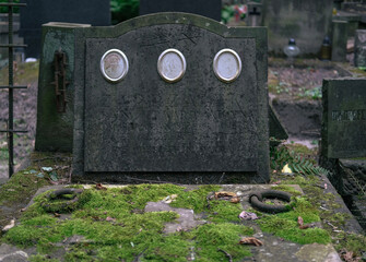 Aged gravestone with moss-covered surface and three faded portrait medallions in a historic...