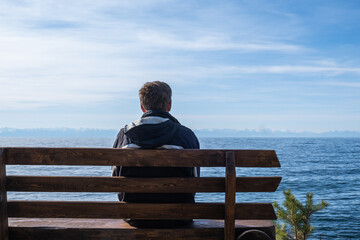 person is seated on rustic wooden bench overlooking calm body water. sunlight casts warm glow as...