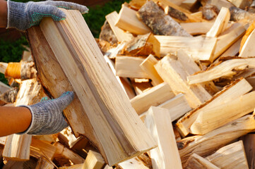 A person in cotton gloves is holding a log for kindling the fireplace or stove, and there are many...