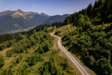 Aerial mountainous landscape with meandering path through lush green French Alps valley tourist destination winter sports near Les Gets village with rocky mountain top against a clear blue sky. 