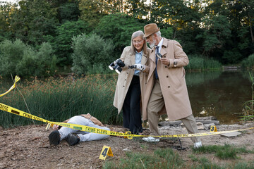 Forensic expertise. Detectives working at crime scene with dead man's body near lake outdoors