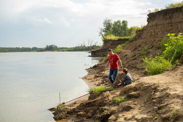 Fototapeta premium Grandfather is teaching a grandson fishing on the river beach.