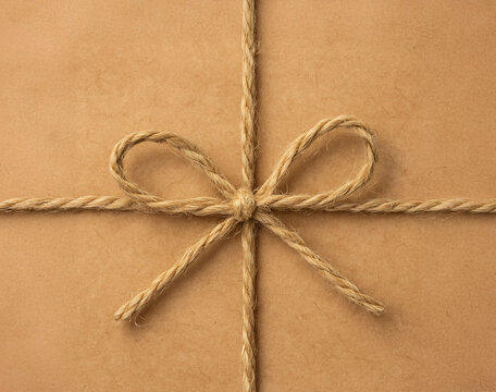 Close-up of natural jute twine tied in a bow on kraft paper package. Minimalistic eco-friendly gift wrapping, rustic and sustainable packaging concept.