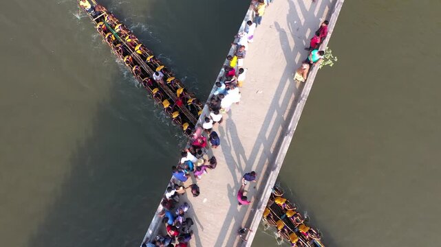 Bogura, Bangladesh - 22 August 2025: Aerial view of boats racing under a bridge packed with onlookers, their vibrant colors contrasting with the dark water.