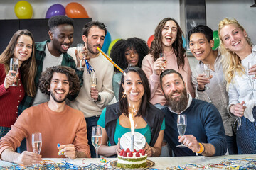 Group of young multiethnic friends celebrating a birthday with cake, balloons, and champagne in a joyful indoor party. Millennials and gen z enjoying fun, diversity and friendship.