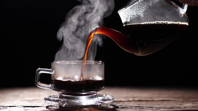 Coffee. Hot coffee being poured into a clear glass cup with steam rising against a dark background, symbolizing warmth, freshness, and energy. Concept of hot coffee drink.