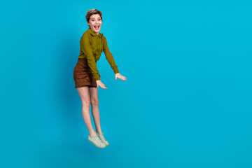 Young woman with short hair jumps joyfully wearing a khaki shirt and brown skirt against a vibrant...