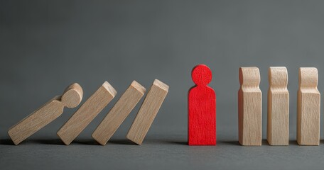 Domino effect on wooden figures, highlighting a unique, red one resisting collapse