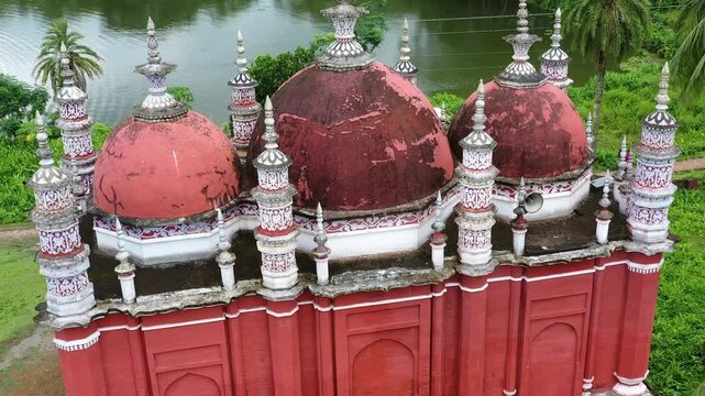 Barishal, Bangladesh - 22 August 2025: Aerial view of the Baitul Aman Jame Masjid, its red domes contrasting with the lush green trees surrounding the mosque.