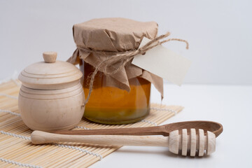 Jar of honey with wooden honey dipper on white kitchen background. Tasty honey bunker.