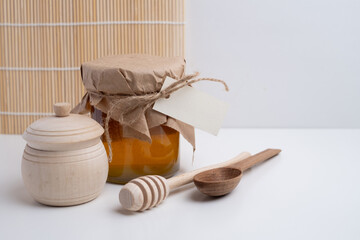 Jar of honey with wooden honey dipper on white kitchen background. Tasty honey bunker.