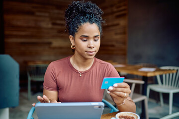 Focused young woman using tablet and credit card, making online payment while enjoying a coffee...