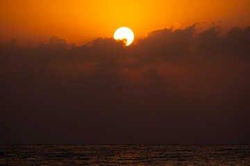 Morning sun rising through clouds over water. Sunrise over the sea with clouds. Scenic sunrise with clouds over the sea. Golden sun emerging above ocean at dawn.