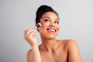 Portrait of a young woman applying makeup with a brush, showcasing natural beauty and skincare