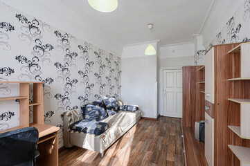 cozy living room features floral wallpaper, a sofa with Asian-style cushions, a desk, and wooden furniture. Two pendant lights illuminate the space