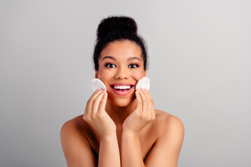Young beautiful woman smiling while cleansing her face, holding soft cotton pads, showcasing skincare