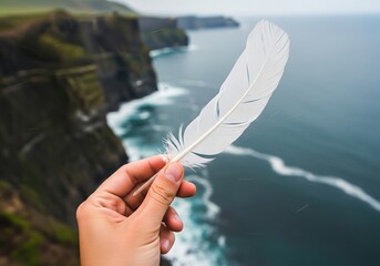 Close-up of a feather held by hand with dramatic cliffside ocean view behind, Ai Generate.