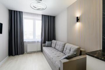 Cozy living room with a grey sofa, dark curtains, a modern light fixture, and a wood-paneled accent wall with sconces