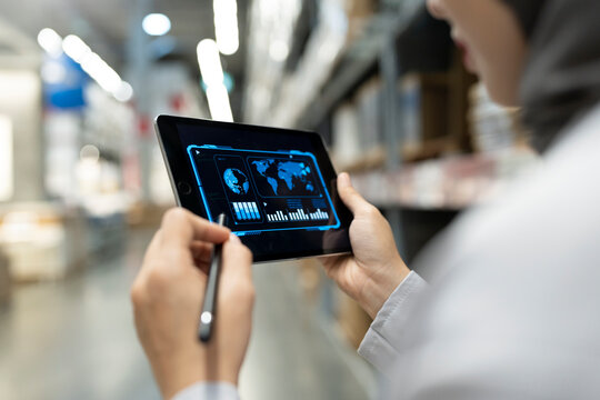 Rear view of Muslim female warehouse worker analyzing business data on tablet PC in warehouse