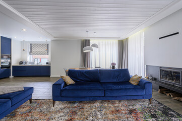 modern living space with a blue velvet sofa, wooden ceilings, and an open kitchen. A fireplace and...